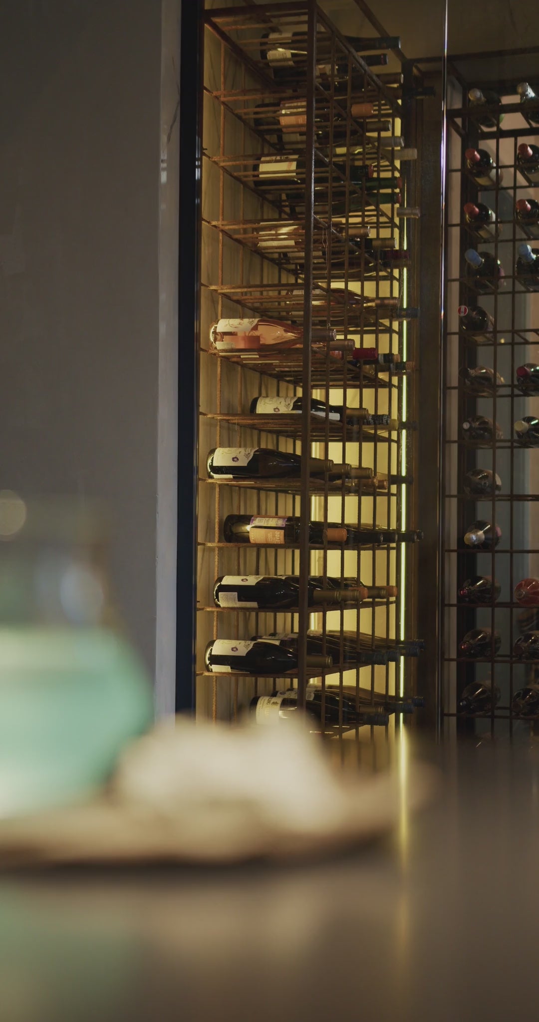 Mur de vin éclairé, bouteilles couchées sur des étagères, lumière chaude
